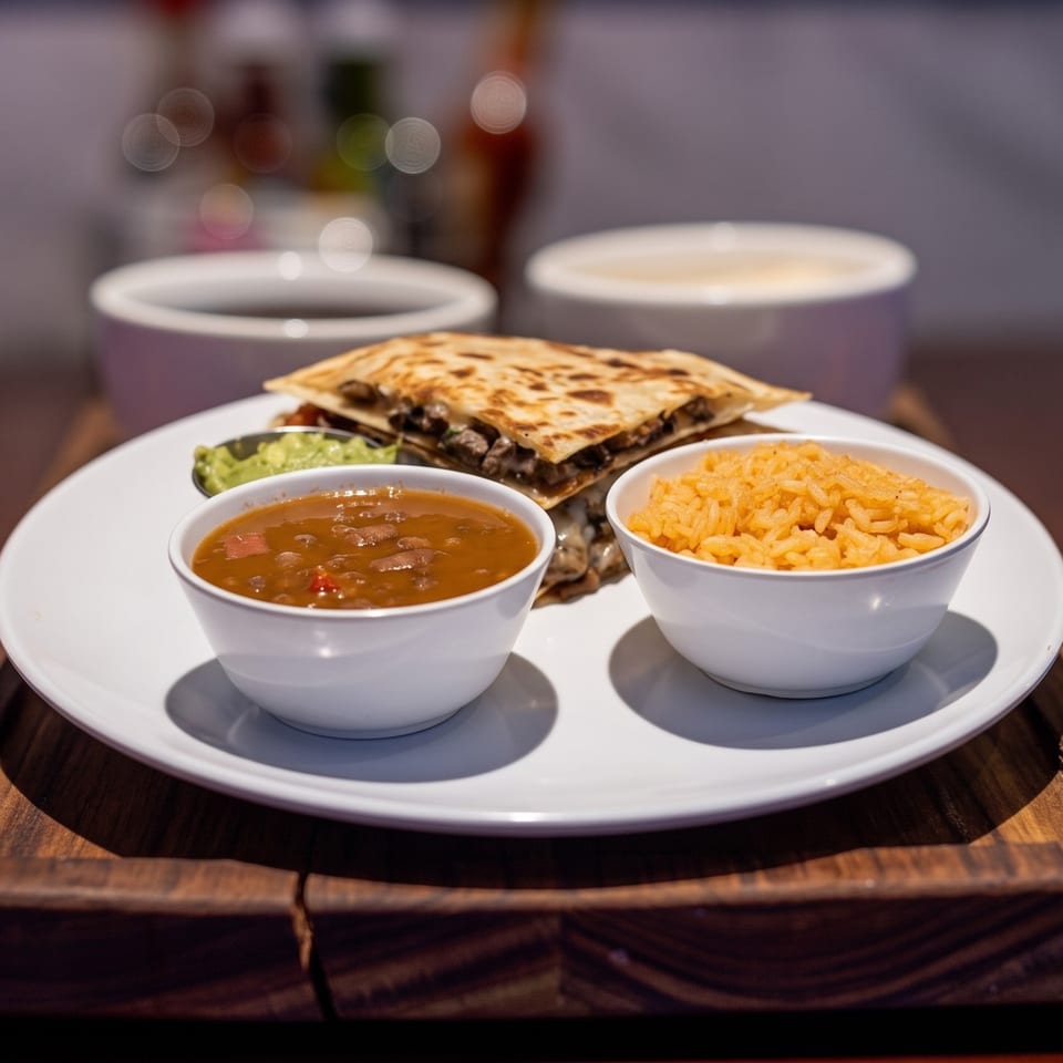 Steak quesadilla with sides of refried beans, rice, and guacamole on a white plate.