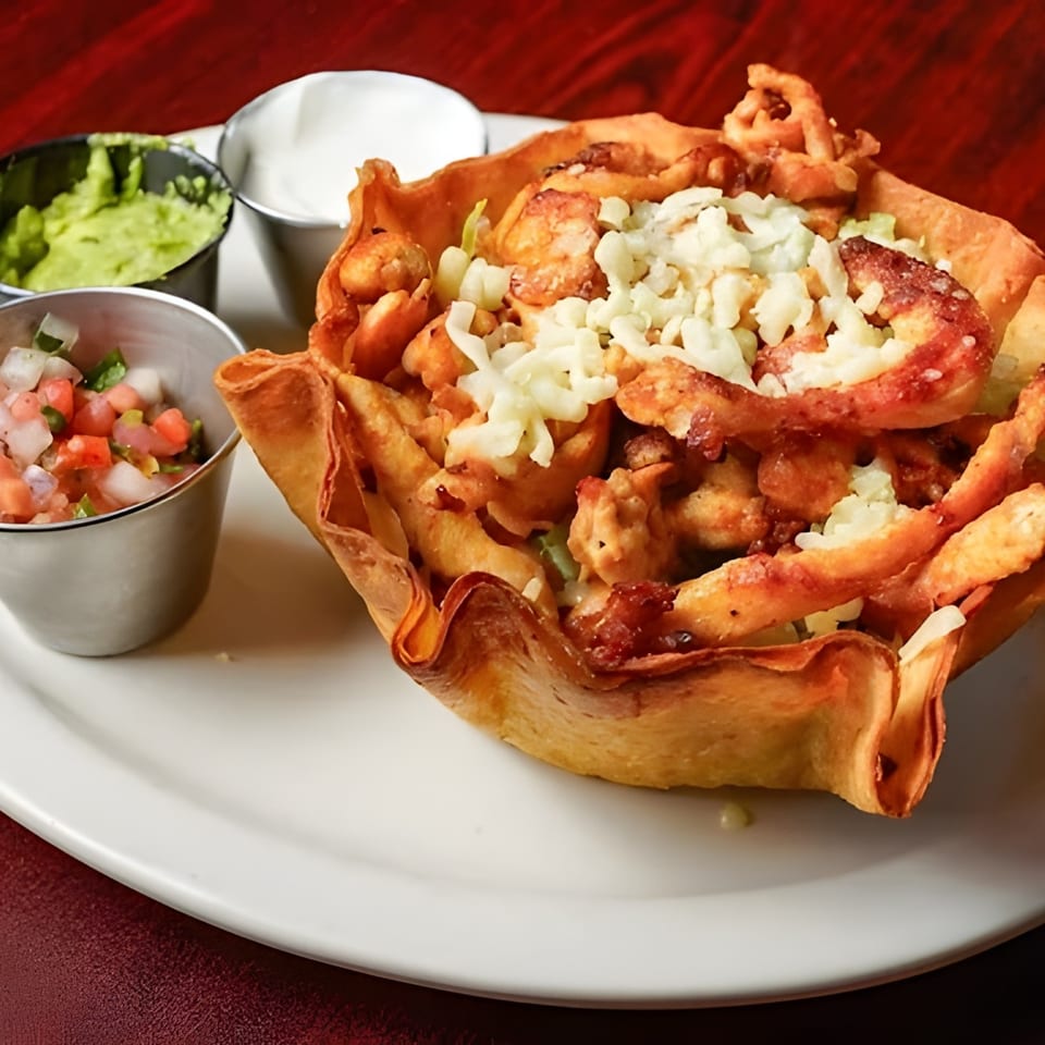 Chicken taco salad in a crispy tortilla bowl with sides of guacamole, pico de gallo, and sour cream.